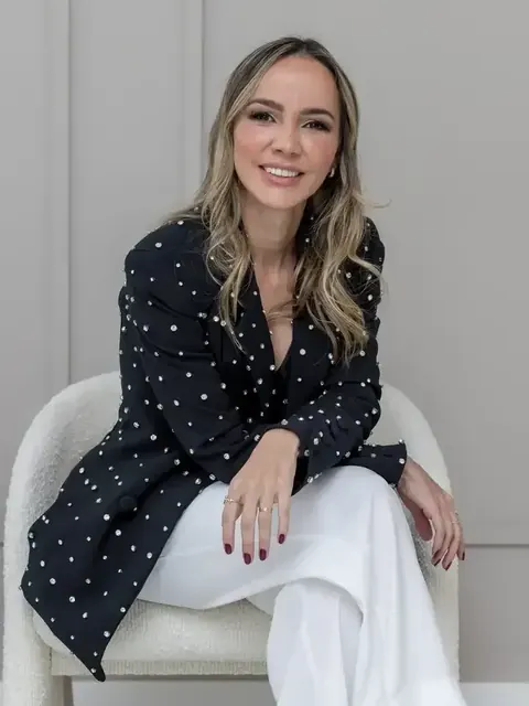 Dra. Mirele Fadel sentada em uma poltrona clara, de blazer escuro